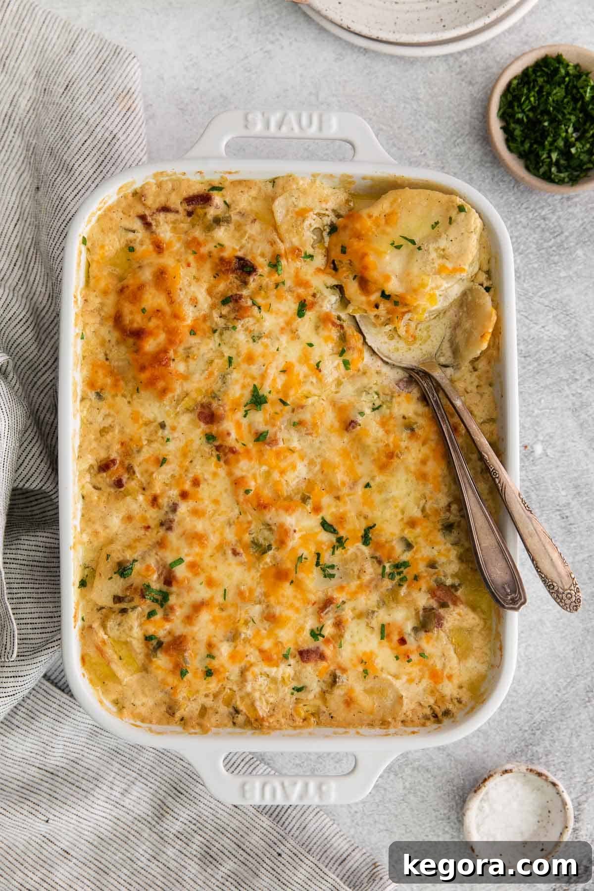 Golden brown scalloped potatoes in a large baking dish, with a serving spoon scooping a portion, highlighting the creamy layers