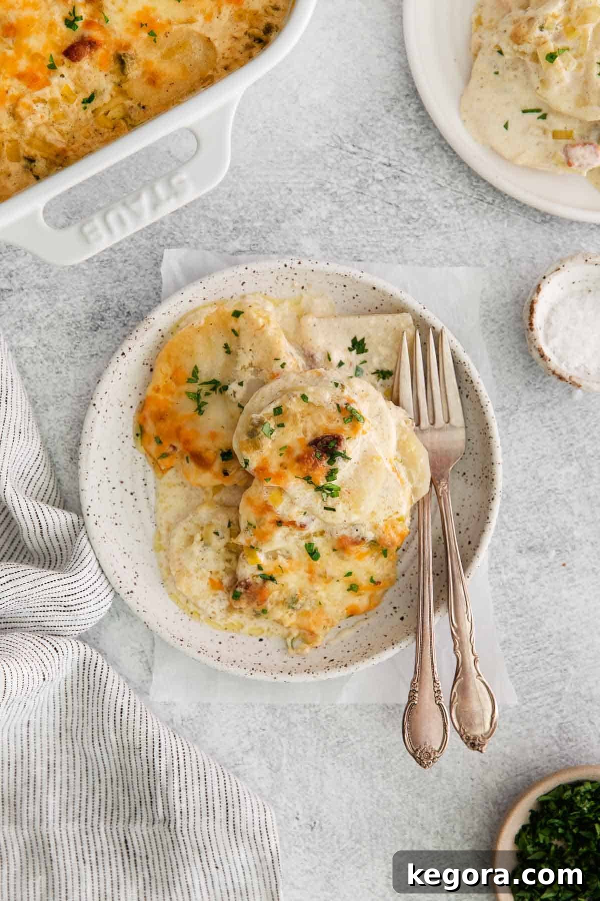 A portion of creamy, cheesy scalloped potatoes served on a white plate with a fork, showcasing the rich texture and golden top.