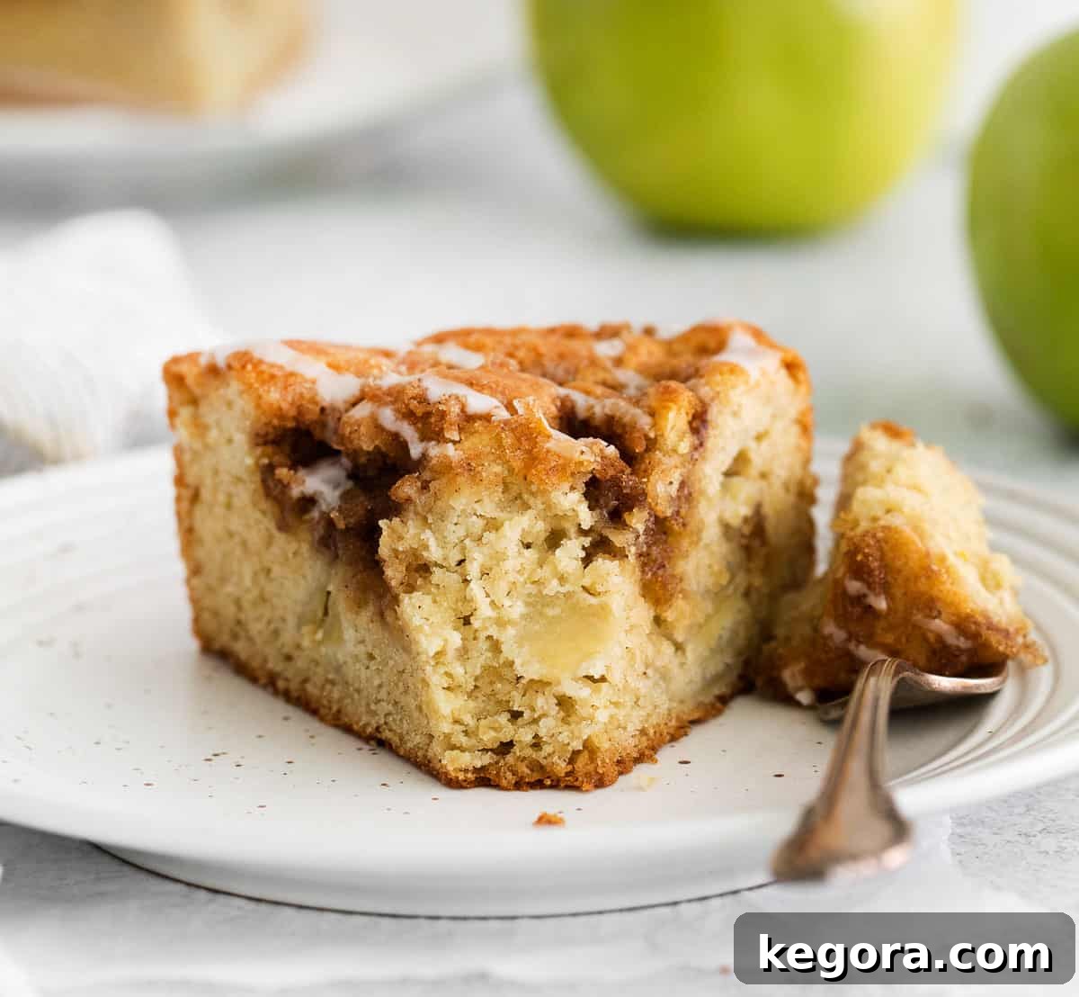 Homestyle Gluten-Free Apple Cake 13 A close-up of a slice of gluten-free apple cake on a plate with a fork, showing the moist crumb and apple pieces.