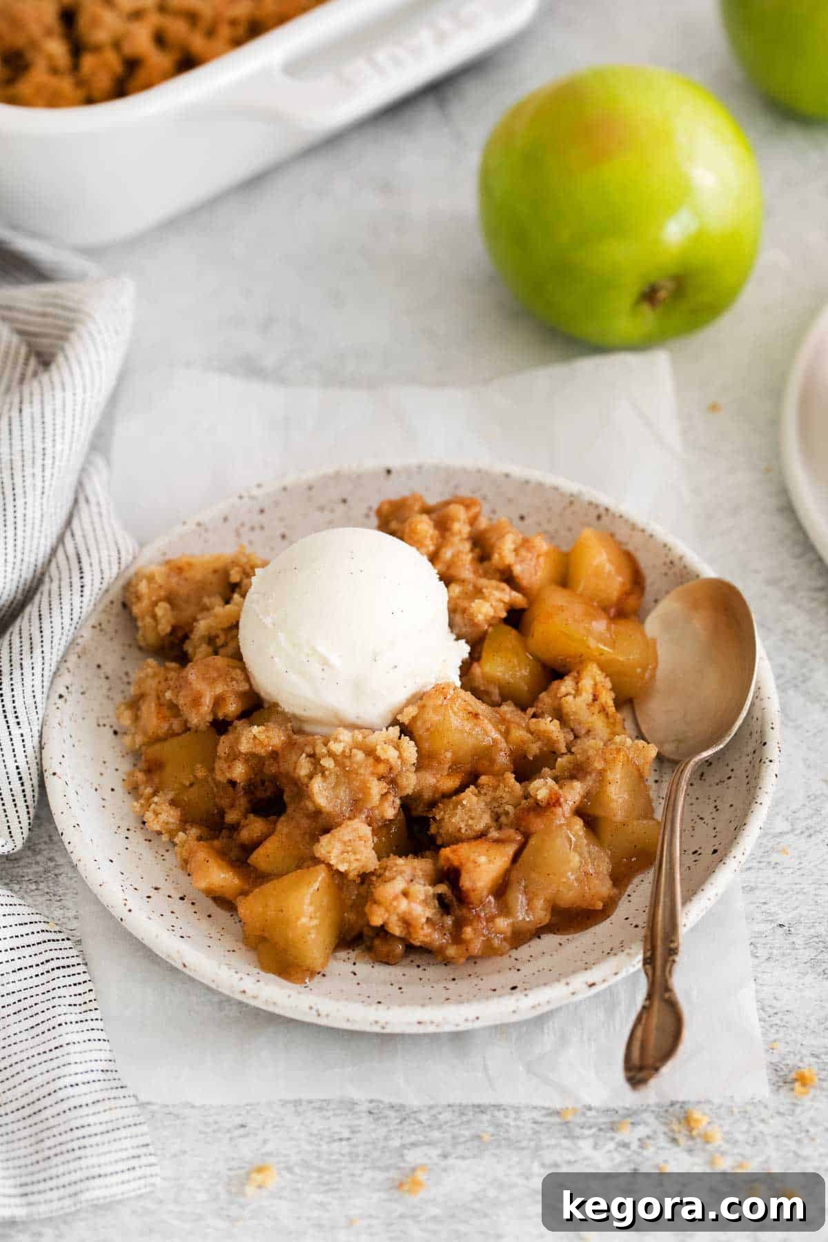 A serving of gluten-free apple crumble on a plate, with a scoop of vanilla ice cream on top and a spoon next to it