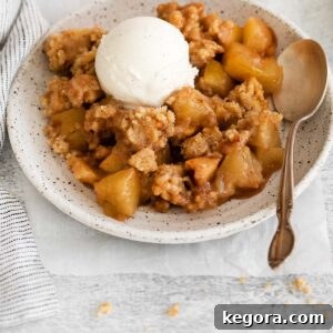 Gluten-free apple crumble on a plate with a spoon next to it and a scoop of ice cream on top