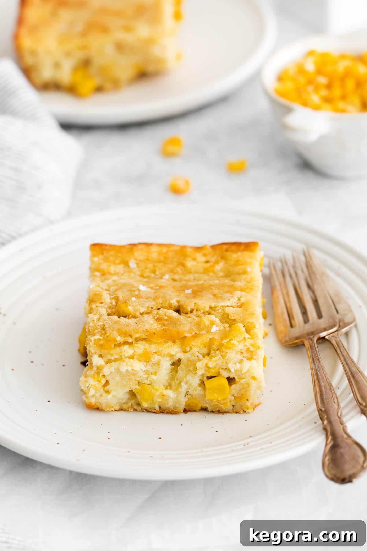 Creamy Gluten-Free Corn Bake 10 A perfectly portioned serving of warm, creamy gluten-free corn casserole on a plate with a fork poised beside it, highlighting its appealing texture