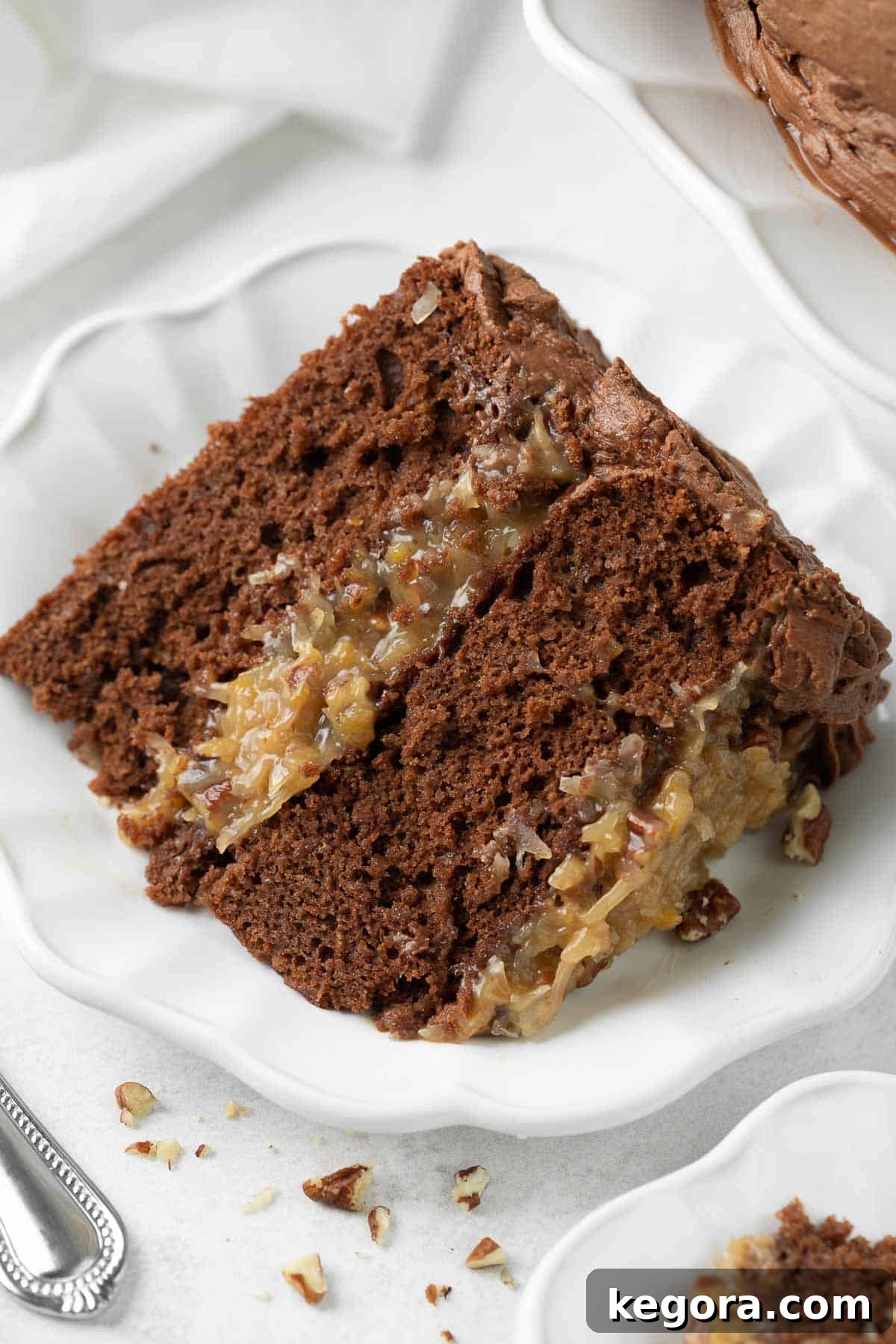 Decadent Gluten-Free German Chocolate Cake 2 A perfectly sliced piece of Gluten-Free German Chocolate Cake on a white plate, showcasing its rich layers of chocolate cake and the signature coconut-pecan frosting.