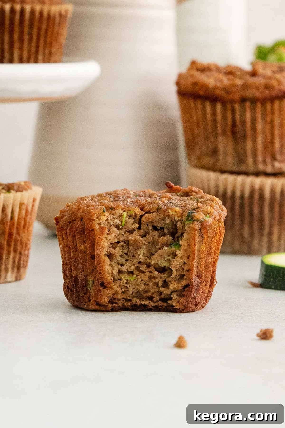 Wholesome Paleo Zucchini Muffins 3 A delicious paleo zucchini muffin with a bite taken out, showing its moist interior, with more muffins blurred in the background.