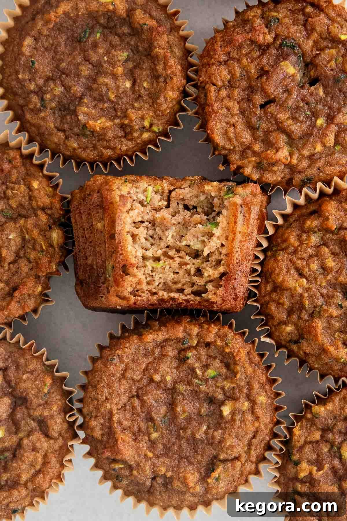 Wholesome Paleo Zucchini Muffins 8 Aerial view of paleo zucchini muffins, with one muffin on its side, showing a bite taken out, on a rustic background.