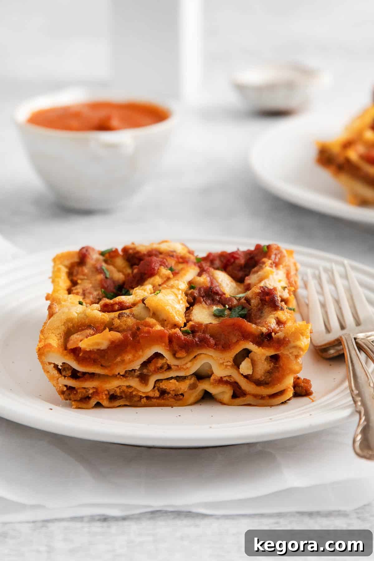 Luscious Dairy-Free Lasagna 10 A perfectly sliced portion of dairy-free lasagna on a white plate, with a fork poised to enjoy the creamy layers.