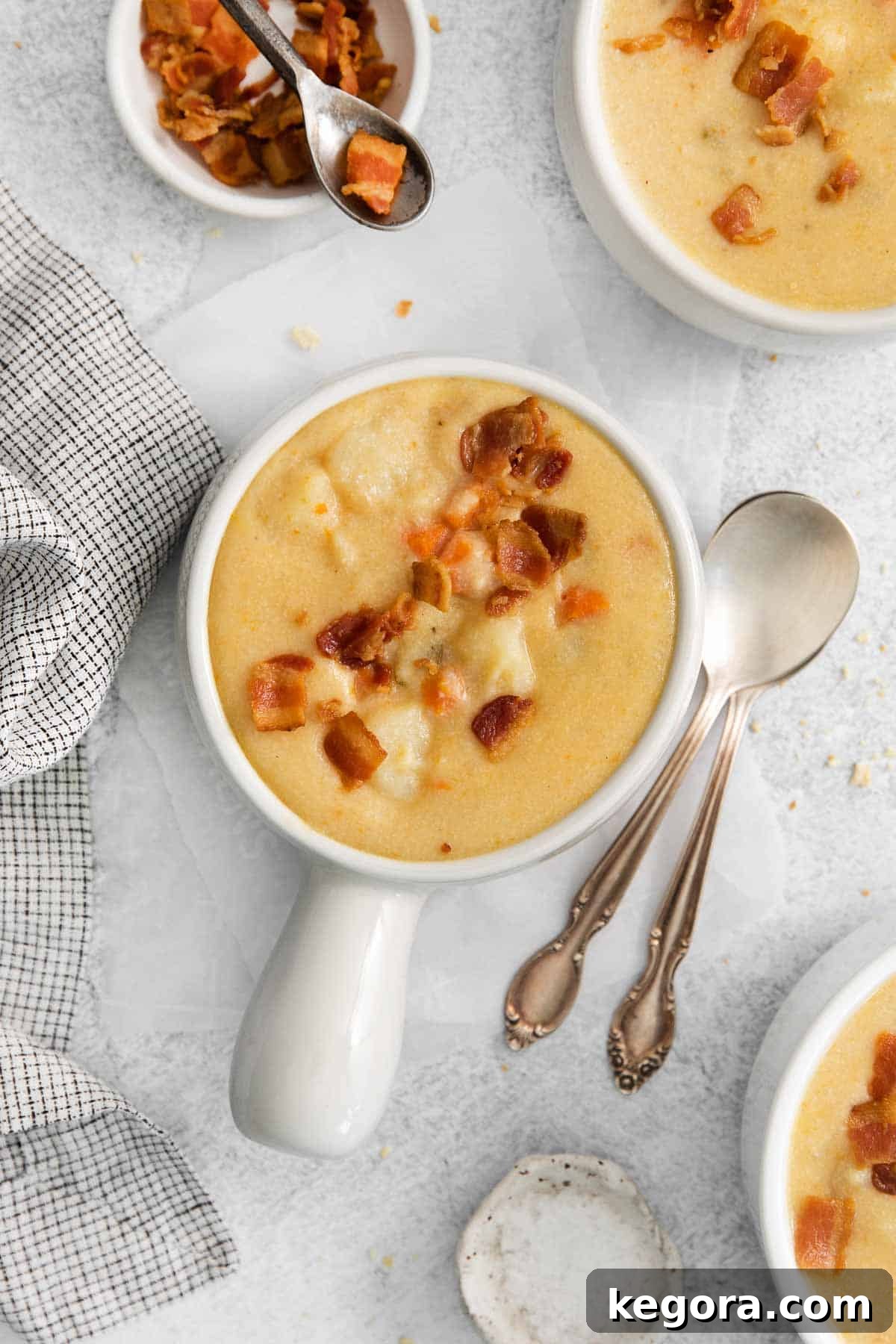 Plant-Based Creamy Potato Soup 3 A steaming bowl of dairy-free potato soup garnished with bacon bits and chives, with a larger pot of soup and more bacon on the side.