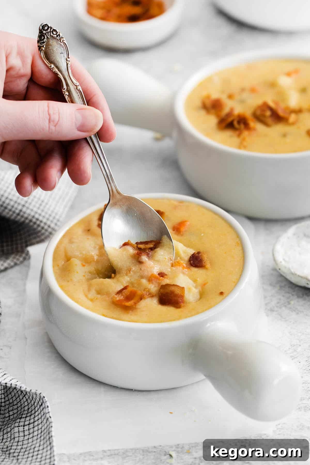 Plant-Based Creamy Potato Soup 8 A close-up of creamy dairy-free potato soup in a bowl, with a hand holding a spoon about to scoop some up.