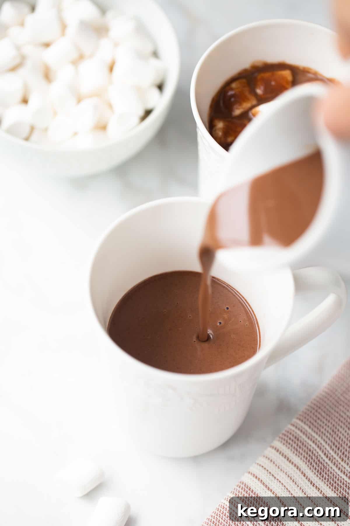 Dairy-Free Hot Chocolate A stream of rich, dairy-free almond milk hot chocolate being poured into a pristine white ceramic mug, promising warmth and comfort.