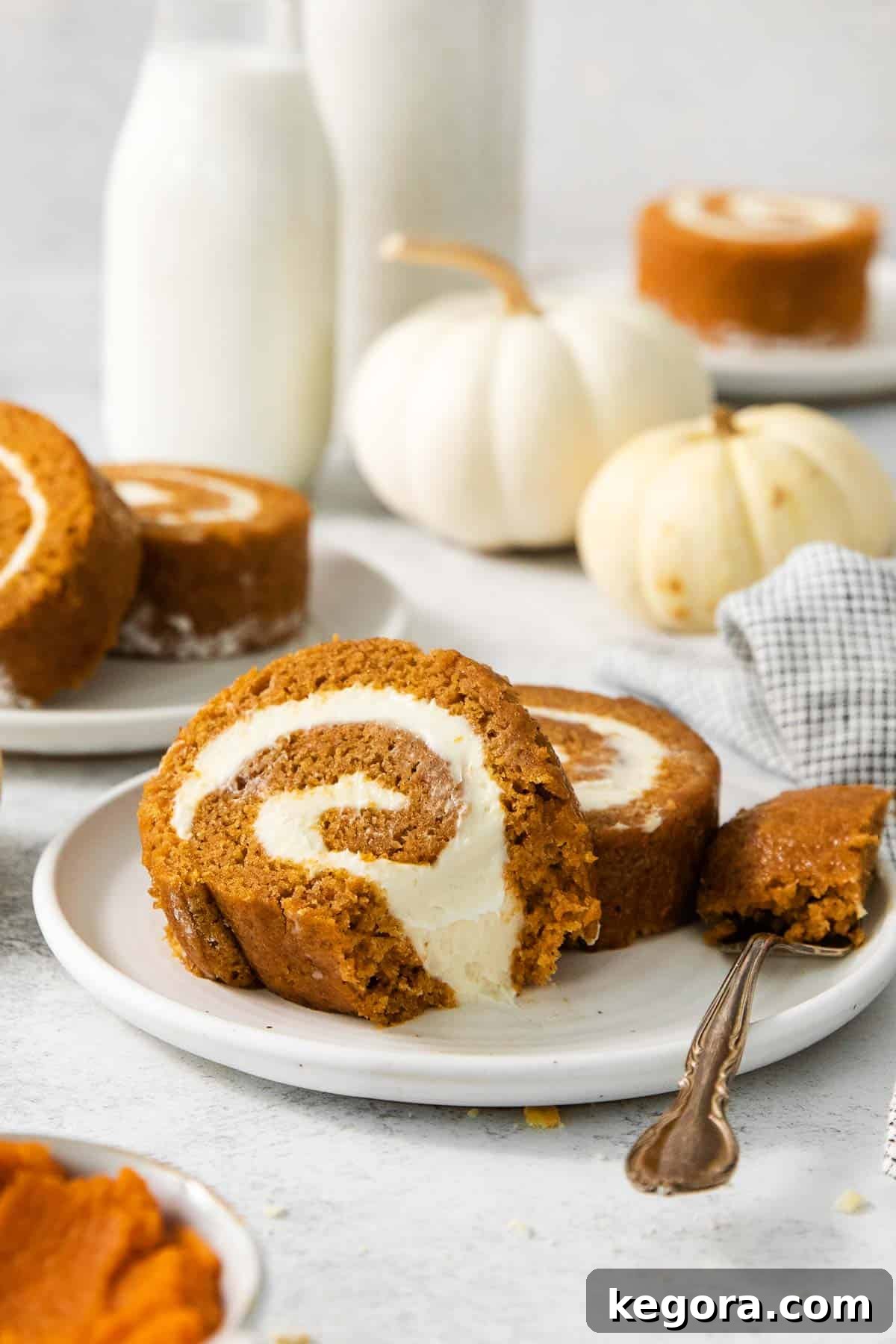 Two perfectly sliced pieces of gluten-free pumpkin roll, featuring moist cake and creamy filling, presented on a white plate with a fork.