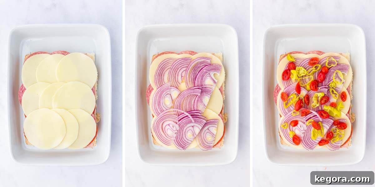 Layering ham, salami, pepperoni, provolone cheese, red onion, cherry tomatoes, and pepperoncini onto the bottom halves of Hawaiian rolls in a baking dish.
