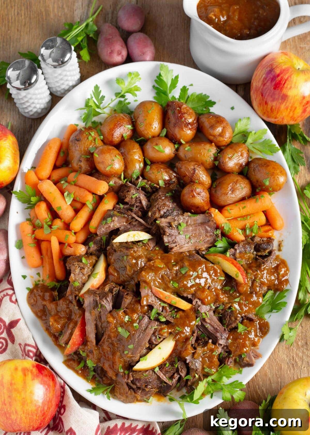 A stunning Apple Cider Pot Roast arranged on a white serving platter, garnished with tender carrots and roasted potatoes.