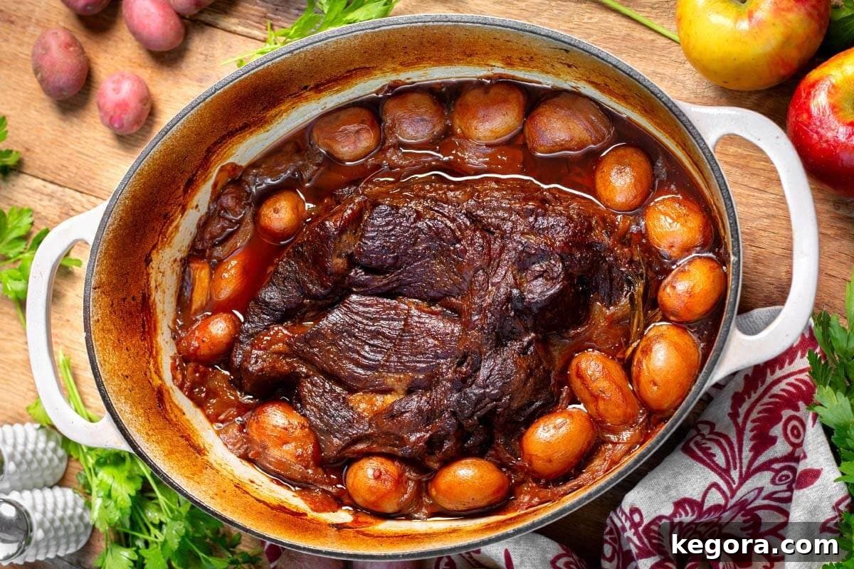 A close-up of Apple Cider Pot Roast nestled among roasted potatoes in a rustic Dutch oven.