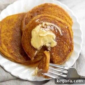 A close-up image of fluffy gluten-free pumpkin pancakes on a white plate, topped with a pat of butter and syrup.