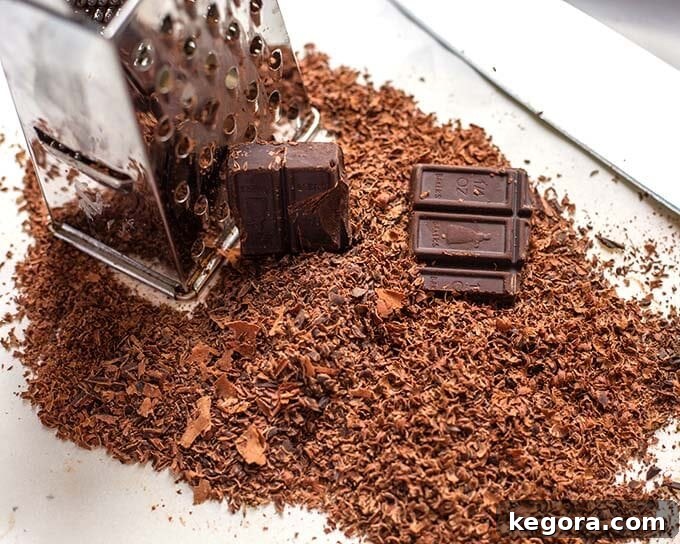 Close-up of a grater with freshly grated bittersweet baking chocolate, illustrating the texture and quality that enhances the muffins' rich flavor profile.