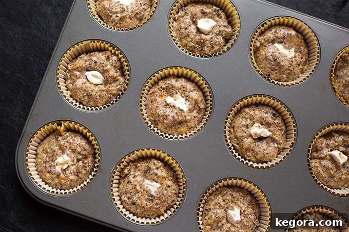 Uncooked Orange Chocolate Cream Cheese Muffins nestled in a muffin pan, showcasing the golden batter ready for baking and the perfectly placed dollops of creamy filling.