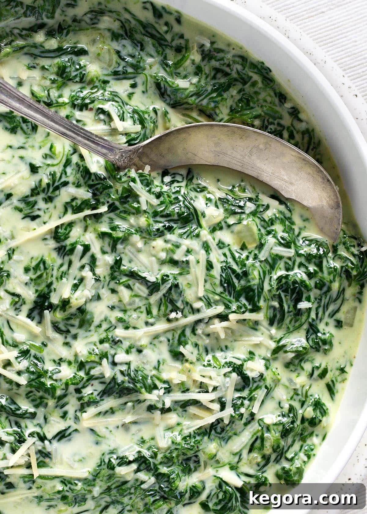 Rich Creamy Cheesy Spinach 2 A close-up shot of creamy, cheesy spinach in a white bowl with a serving spoon, highlighting its rich texture and melted cheese.
