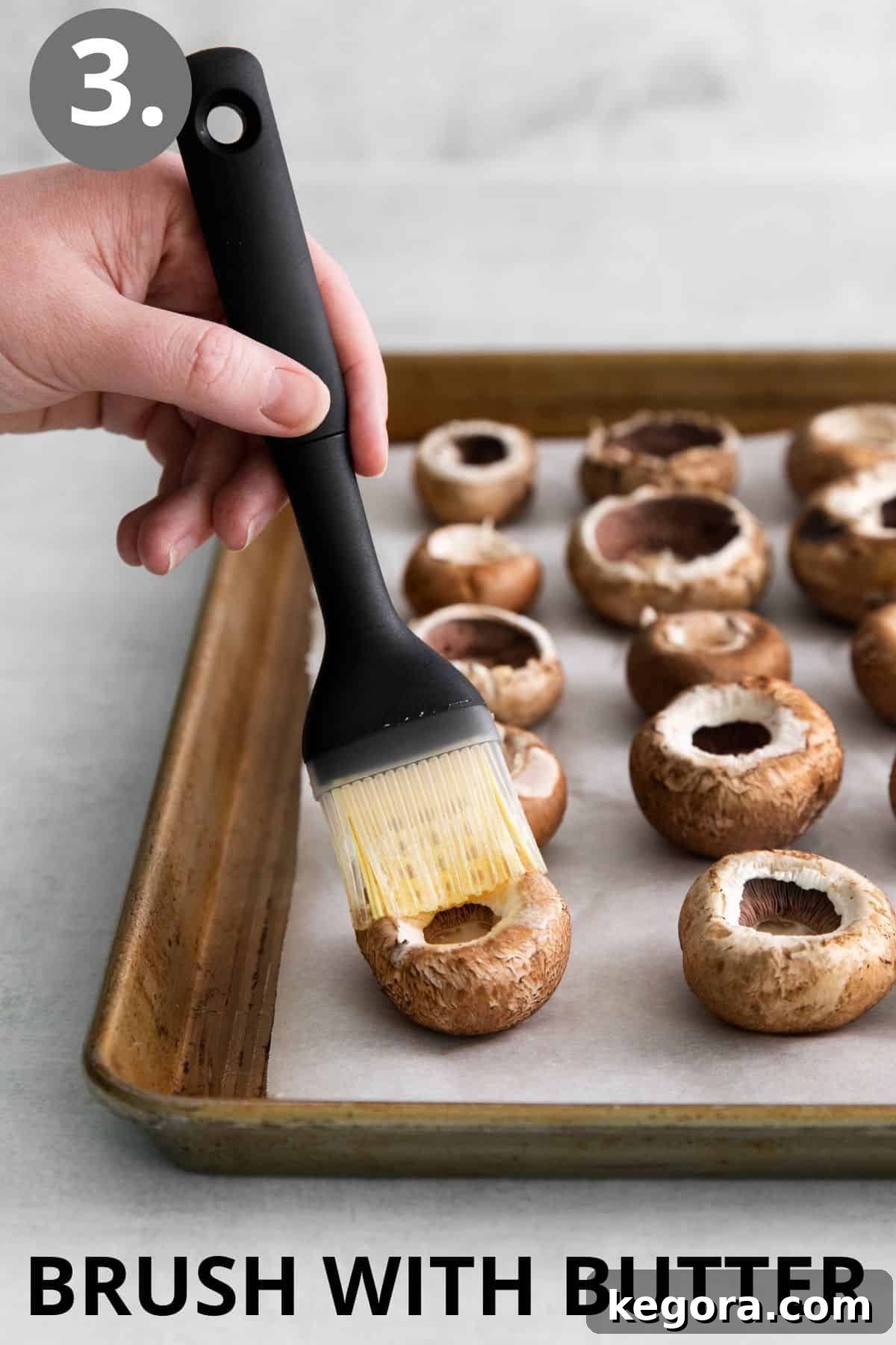A hand brushing melted butter onto a mushroom cap using a silicone basting brush.