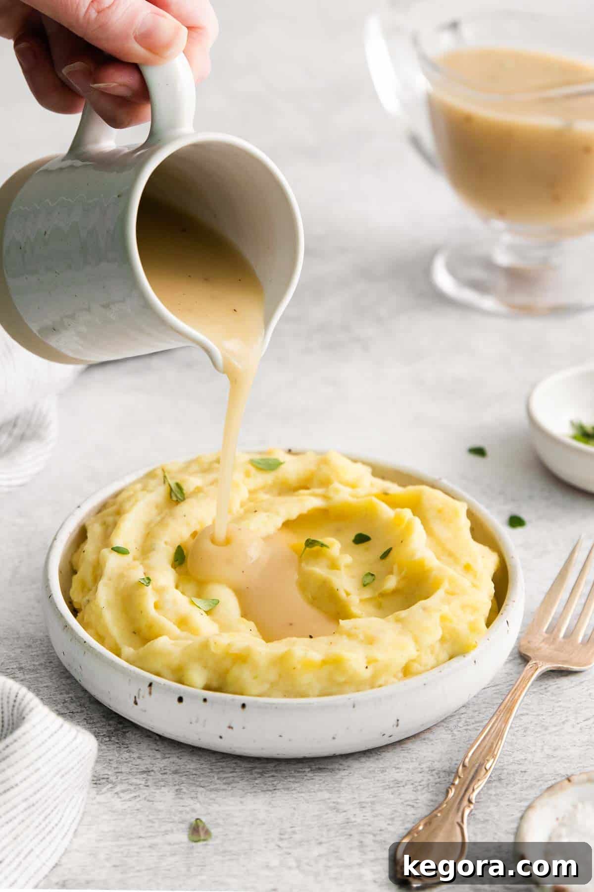 Thick, rich gluten-free gravy being poured generously over a mound of creamy mashed potatoes in a serving dish.