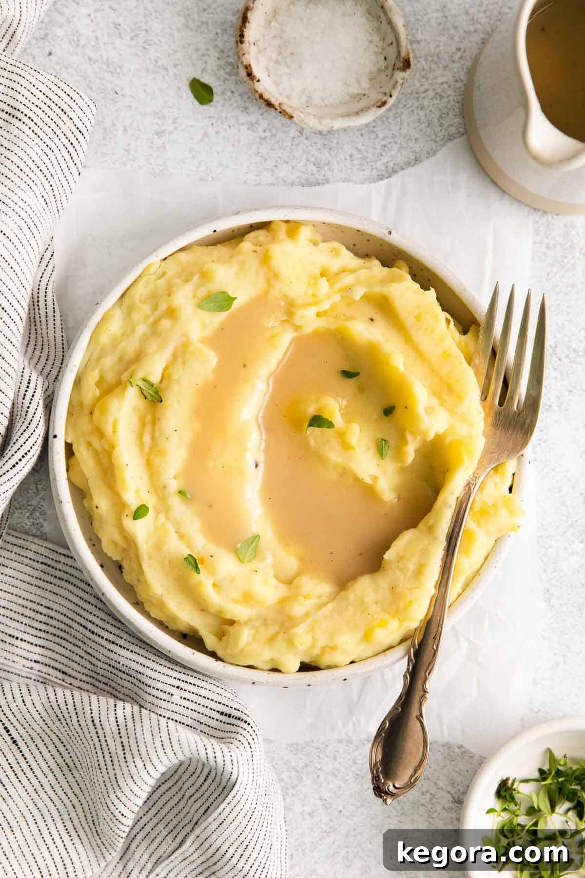 A plate of fluffy mashed potatoes generously topped with rich, savory gluten-free gravy, with a fork resting beside it.