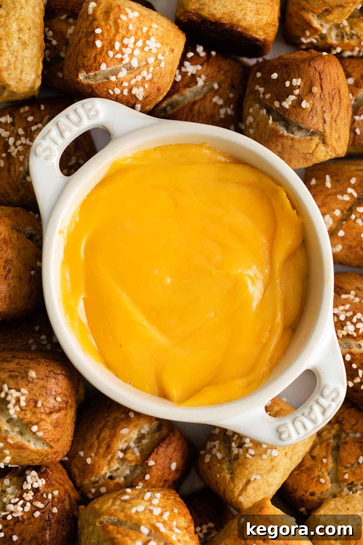 A close-up photo of warm, golden pretzel bites dipping into creamy gluten-free cheese sauce.