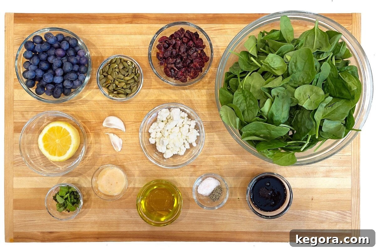 Blueberry Spinach Salad ingredients laid out on a wooden board: spinach, blueberries, dried cranberries, goat cheese, pumpkin seeds, and fresh mint.