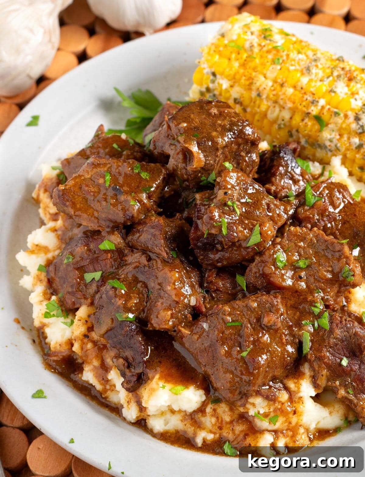 Melt-in-Your-Mouth Slow Cooker Garlic Butter Steak Bites 2 Steak Bites over mashed potatoes on plate with corn.