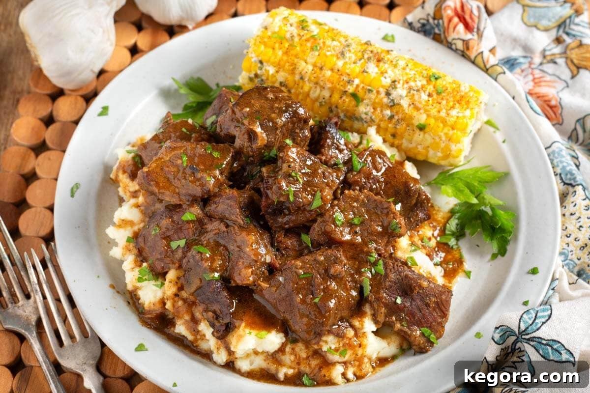 Melt-in-Your-Mouth Slow Cooker Garlic Butter Steak Bites 12 Steak Bites over mashed potatoes on plate with corn.