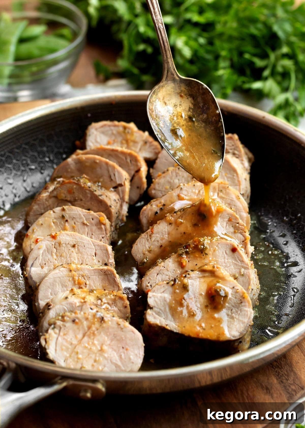 2 Pork Tenderloins sliced in a skillet with spoon drizzling sauce on them.