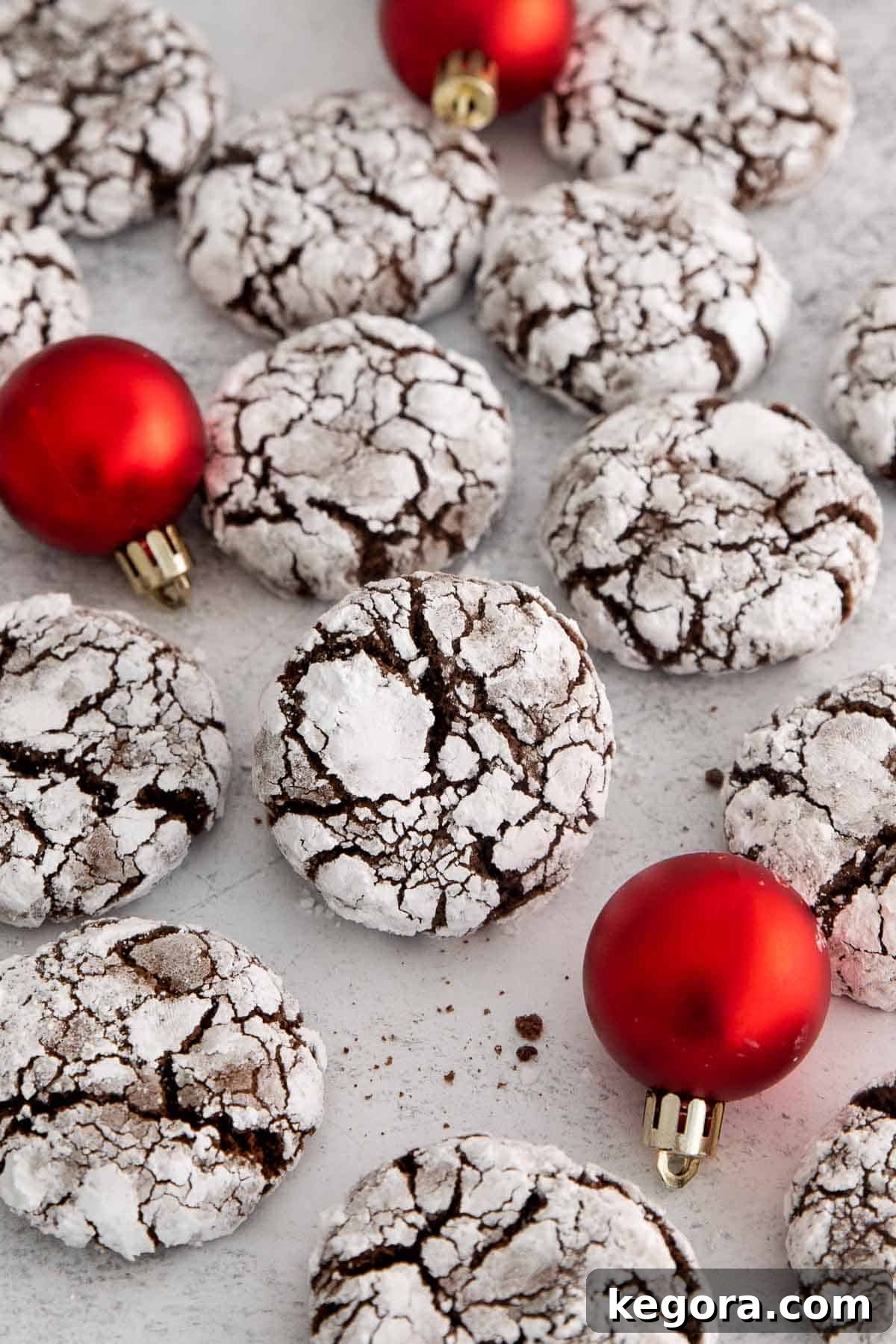 A festive display of gluten-free chocolate crinkle cookies on a countertop, surrounded by red Christmas ornaments.