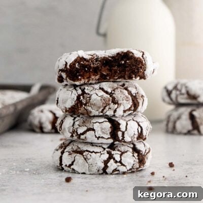 Stack of 4 chocolate crinkle cookies with one bite missing, showcasing the fudgy interior and crinkled exterior.
