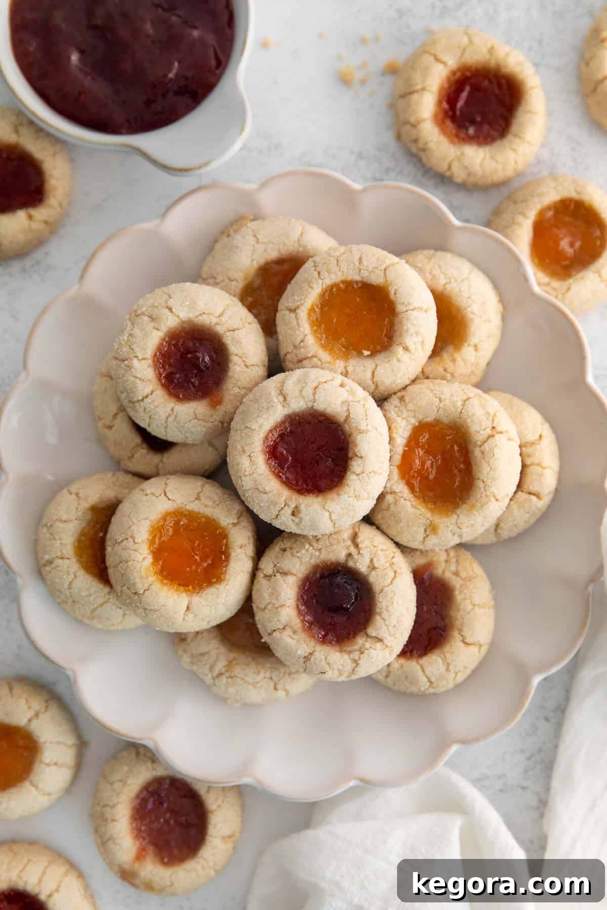 Gluten-Free Thumbprint Delights 3 Stack of jam-filled gluten-free thumbprint cookies on a white scalloped plate, ready to be enjoyed.