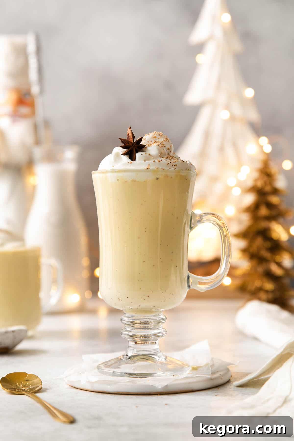 Spiced Dairy-Free Nog Delight 3 A beautifully garnished glass of dairy-free eggnog, with a festive holiday setting in the background, including a softly lit Christmas tree.