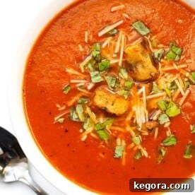 Velvety Instant Pot Tomato Soup 4 Tomato Soup in a white bowl next to silver spoon on a white background, garnished with herbs.