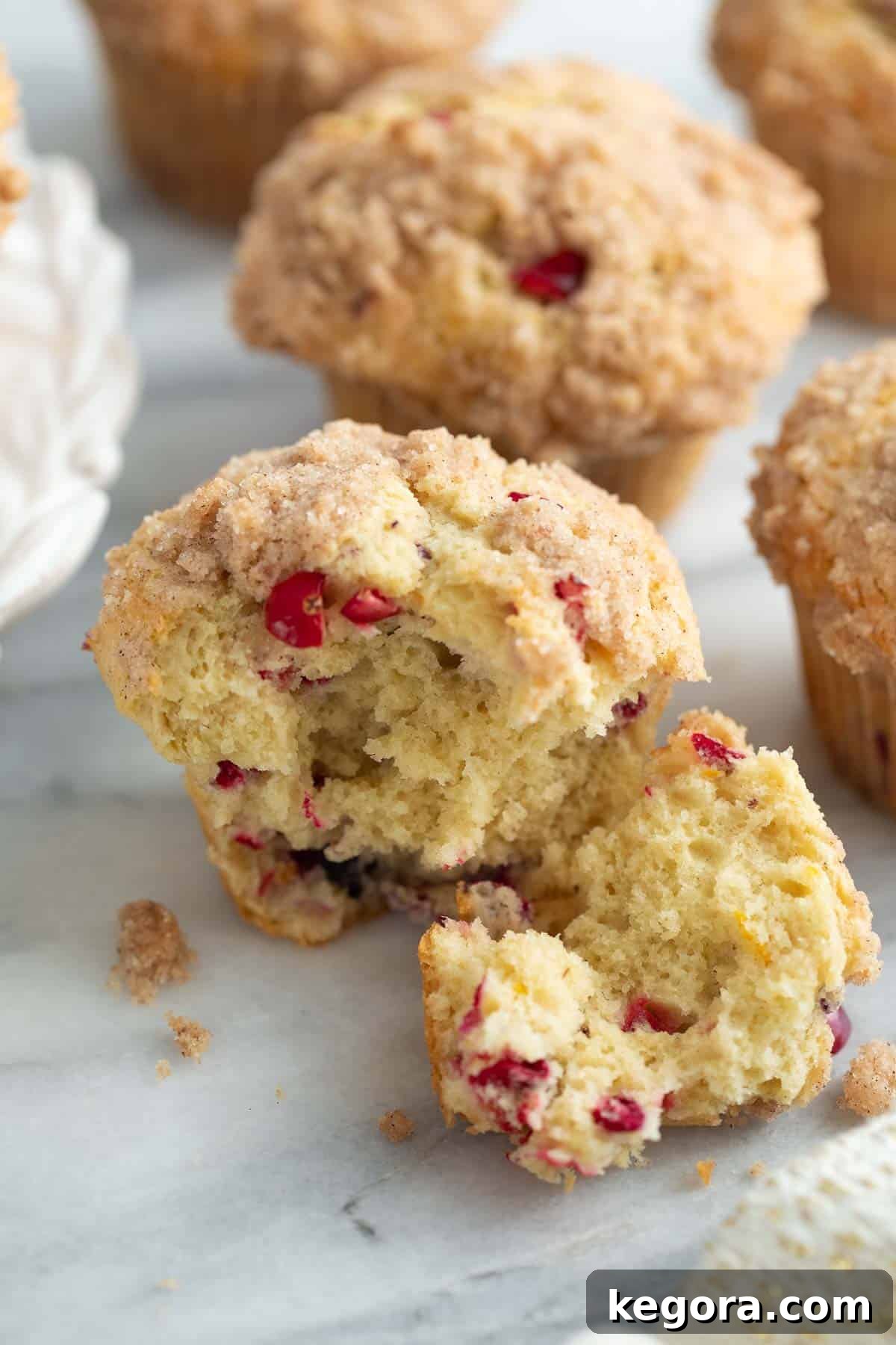Two perfectly baked gluten-free cranberry orange muffins, one with a bite taken out, resting on a marble surface, highlighting their moist interior and crumbly streusel.