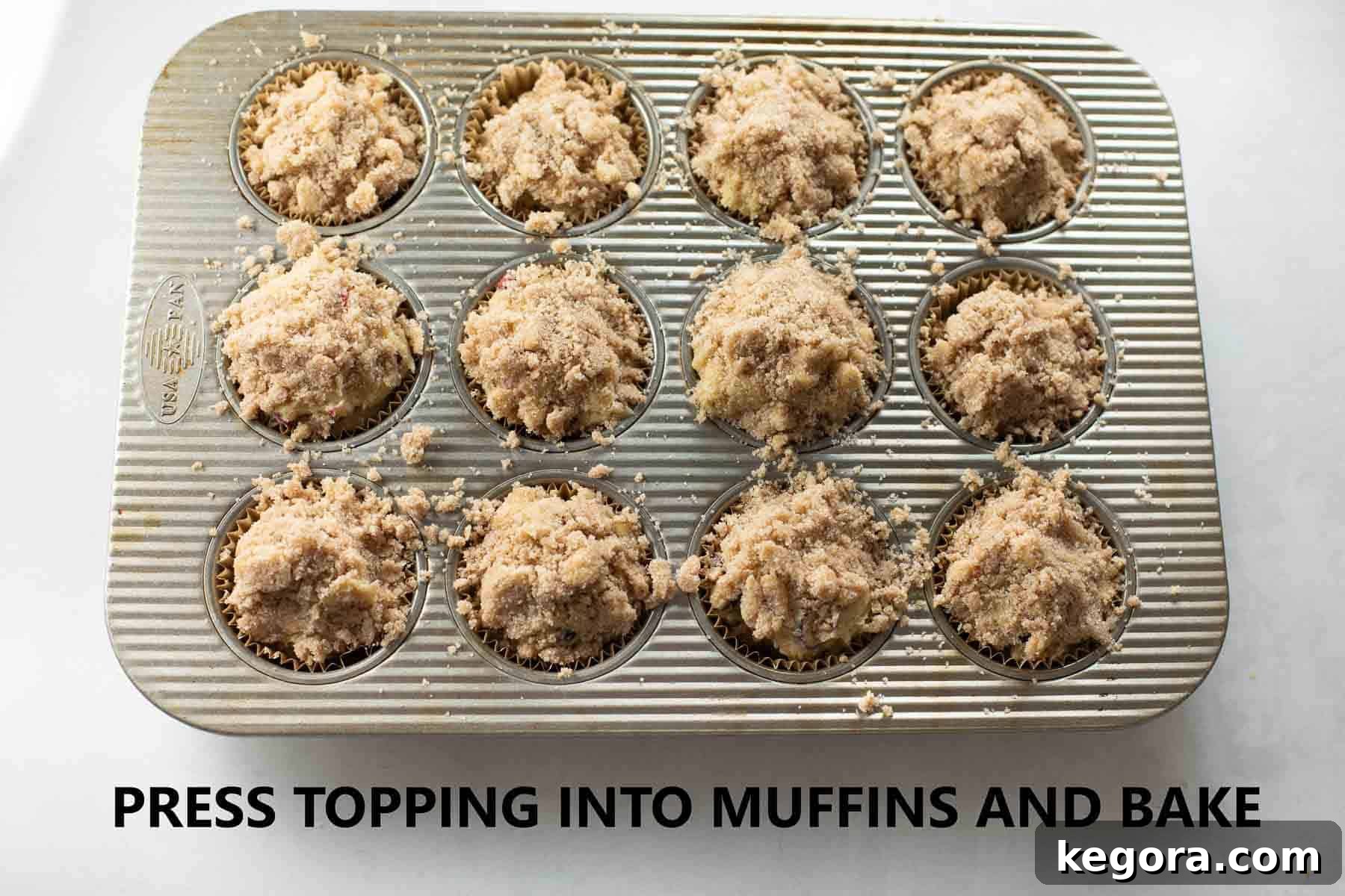 A muffin pan lined with paper cups, each filled with golden batter and topped generously with streusel, ready for the oven.
