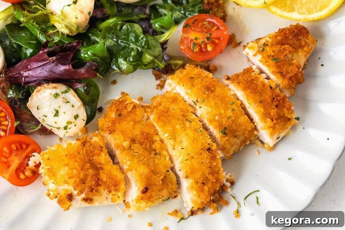 Crispy Skillet Chicken Cutlets 3 Two crispy pan-fried chicken cutlets on a white plate, garnished with fresh parsley and a lemon wedge, beside a vibrant green salad, ready to be enjoyed.