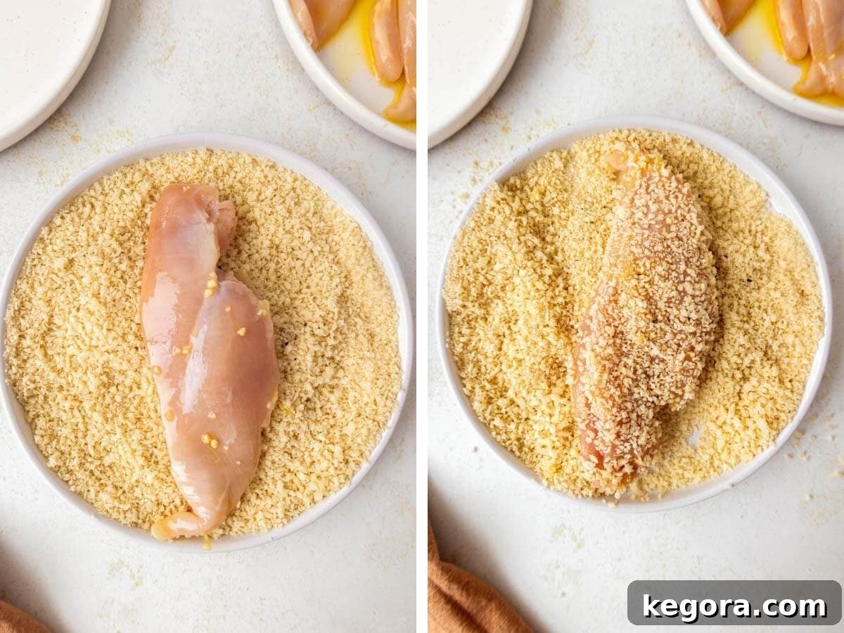 Crispy Skillet Chicken Cutlets 6 Close-up shot of a hand meticulously pressing a raw chicken cutlet into a plate filled with seasoned panko breadcrumbs, ensuring complete and even coverage on both sides.