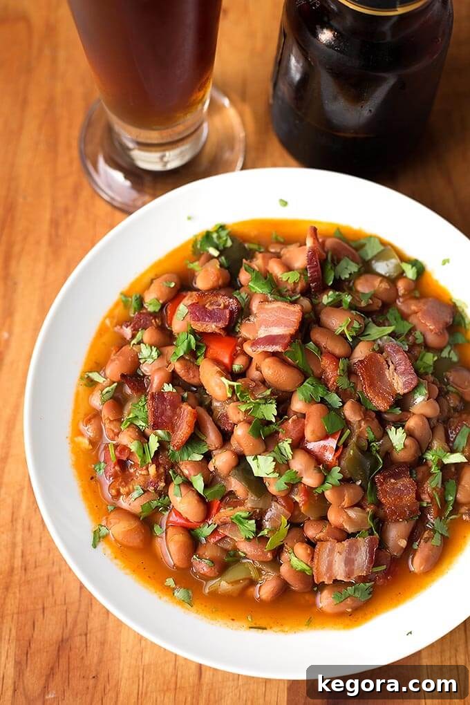 Instant Pot Beer Braised Fiesta Beans 2 Drunken Beans (Frijoles Borrachos), in a white bowl next to glass of beer on a wooden board