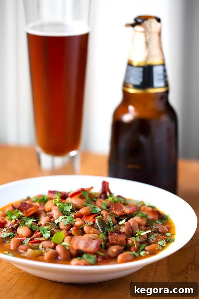 Instant Pot Beer Braised Fiesta Beans 3 Drunken Beans (Frijoles Borrachos), in a white bowl next to glass of beer on a wooden board