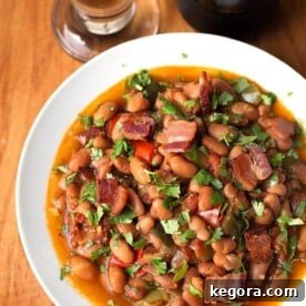 Instant Pot Beer Braised Fiesta Beans 6 Drunken Beans (Frijoles Borrachos), in a white bowl next to glass of beer on a wooden board