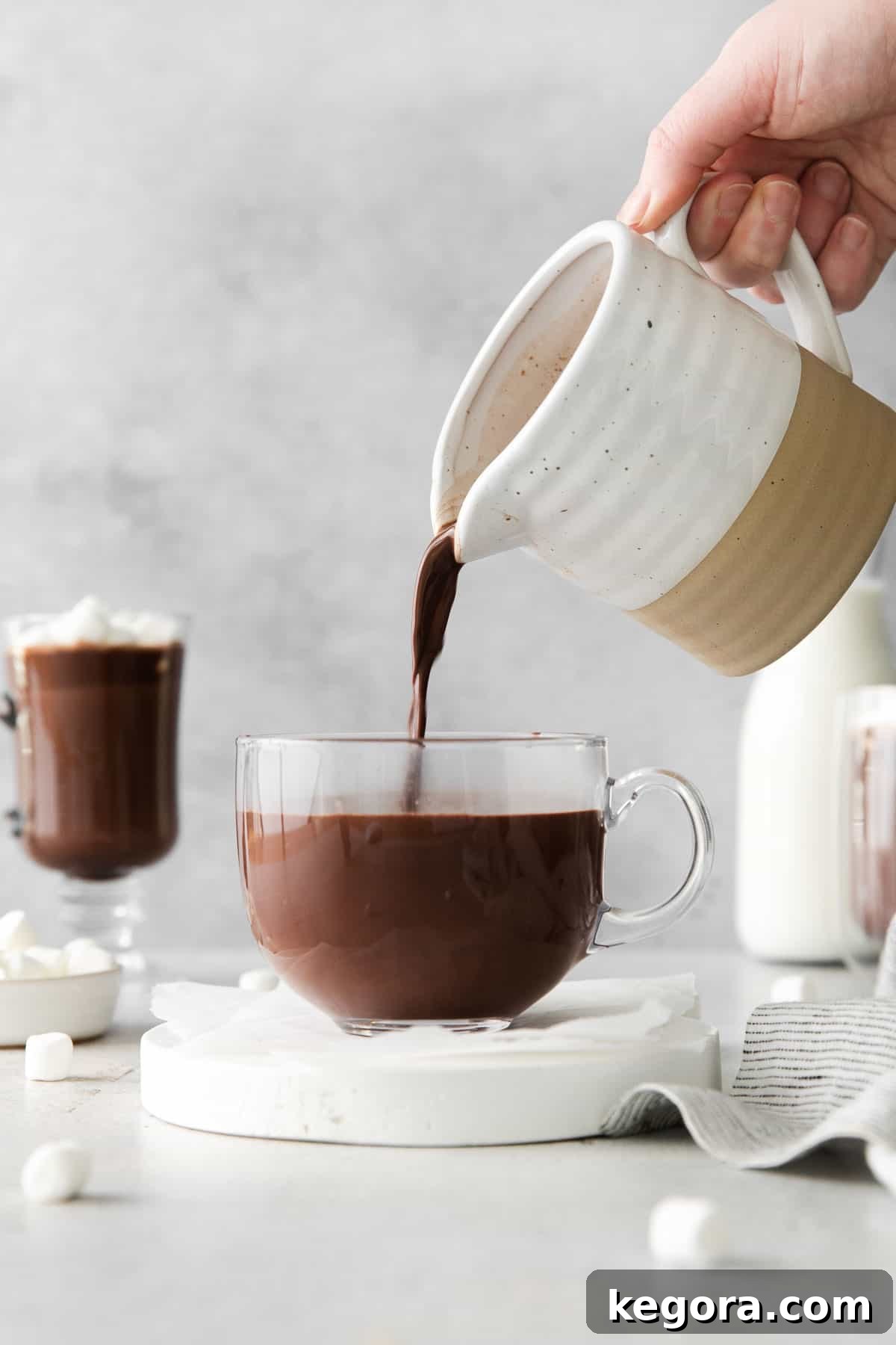 A hand pouring hot chocolate into a glass mug, illustrating the joy of preparation