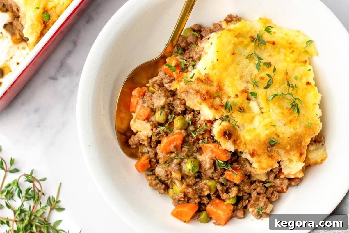 A serving of Irish Cottage Pie in a white bowl with a spoon, garnished with fresh herbs.