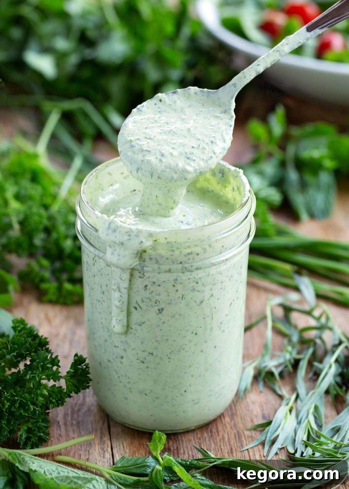 herb yogurt salad dressing in a jar with spoonful above it.