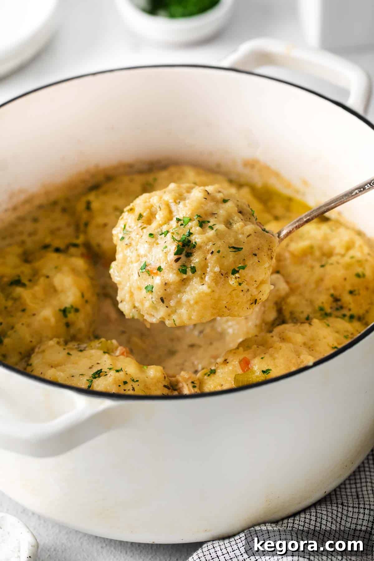A close-up photo of gluten-free chicken and dumplings in a baking dish with a spoon scooping out a serving