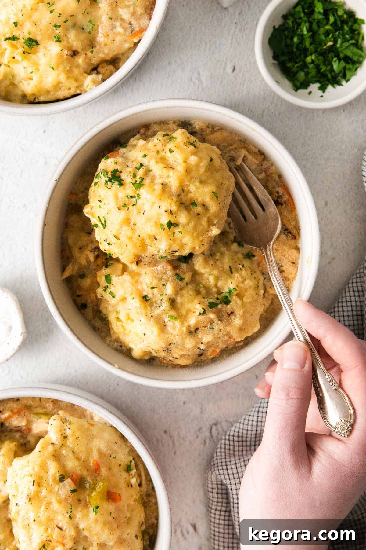 Chicken and dumplings served in a bowl, with a hand holding a fork scooping a portion