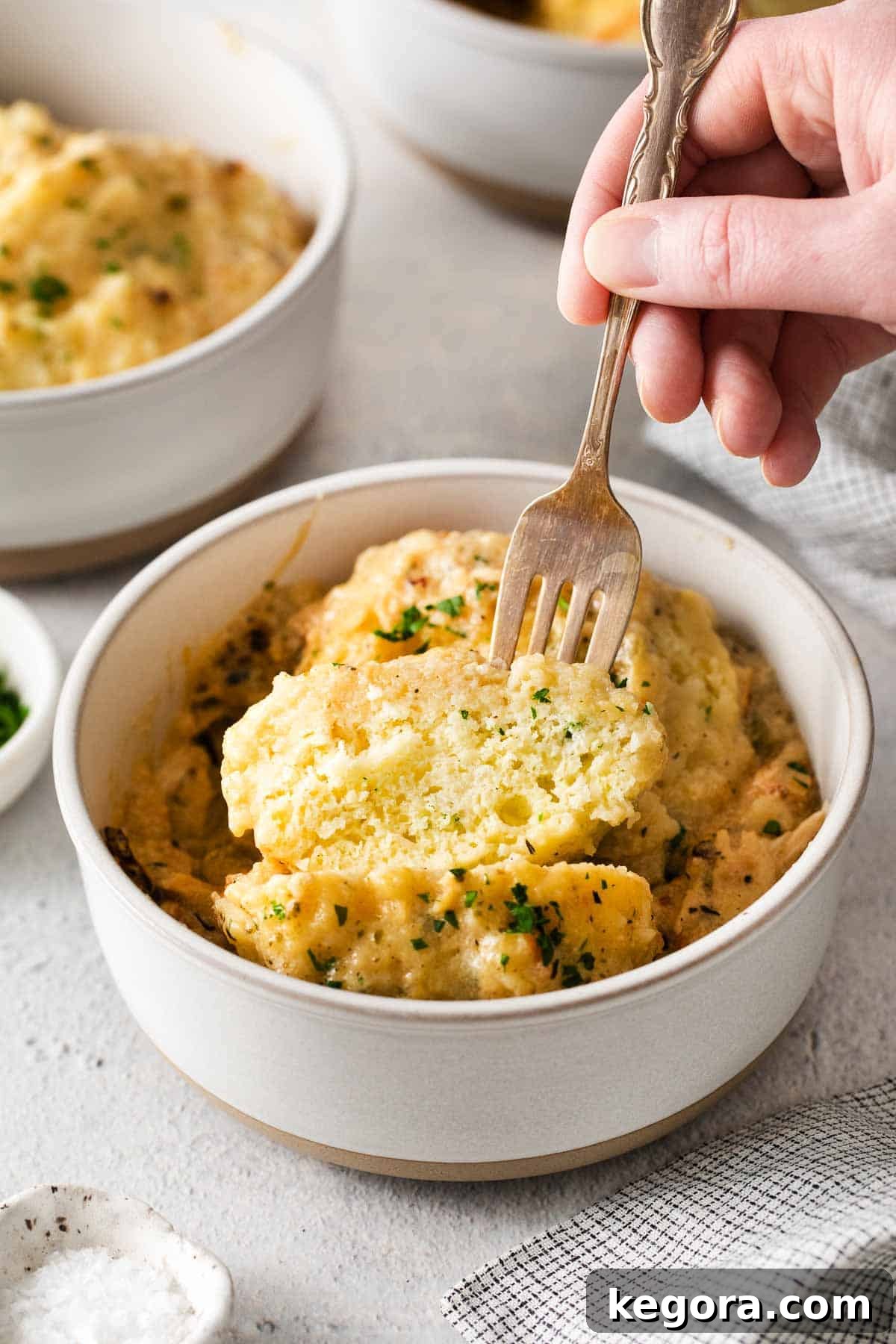 A hand holding a fork and picking up a bite of gluten-free chicken and dumplings