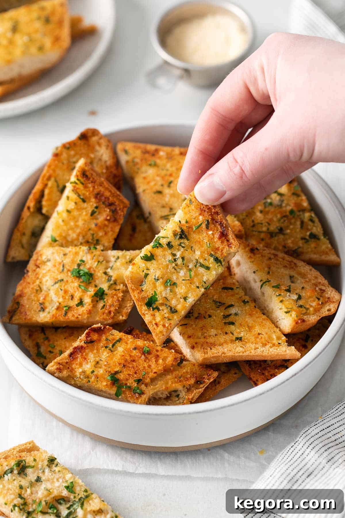 A bowl filled with sliced gluten-free garlic bread, with a hand reaching for a piece, illustrating its inviting nature.