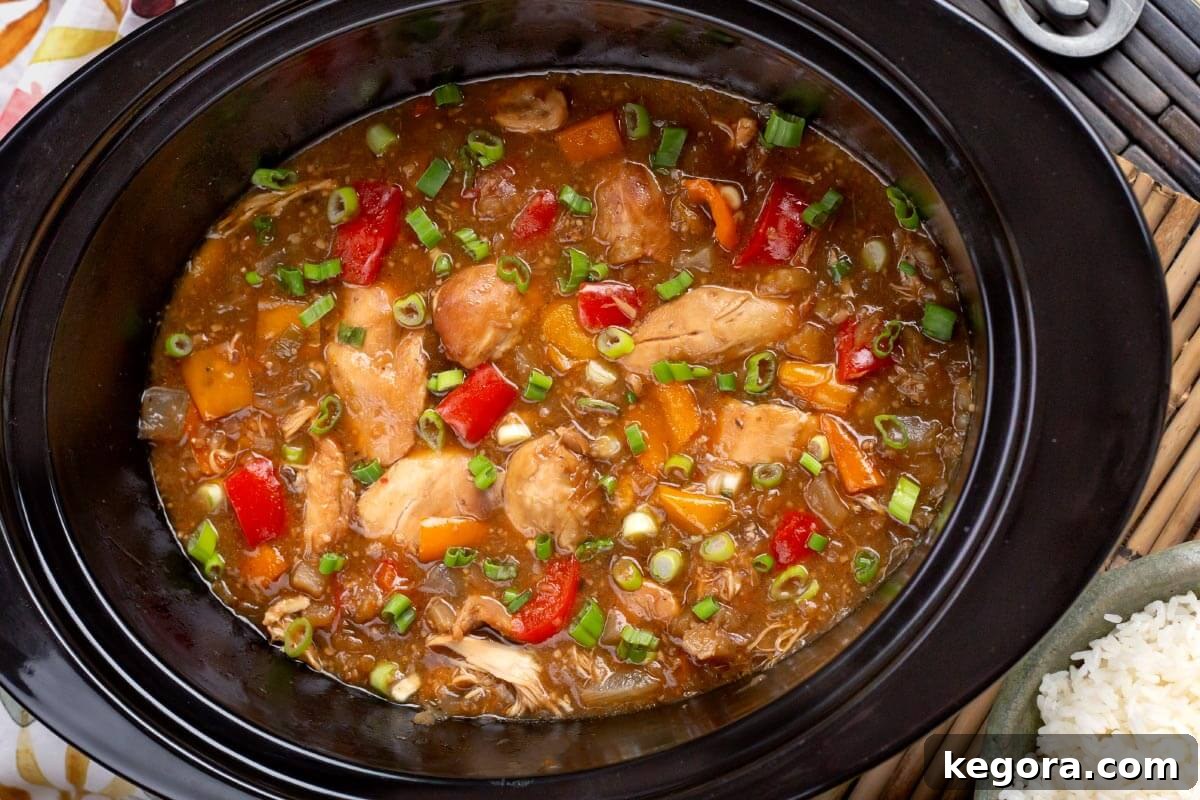 Slow Cooker Pineapple Chicken cooking in a black crock pot, showing the chicken and vegetables simmering in the sauce.