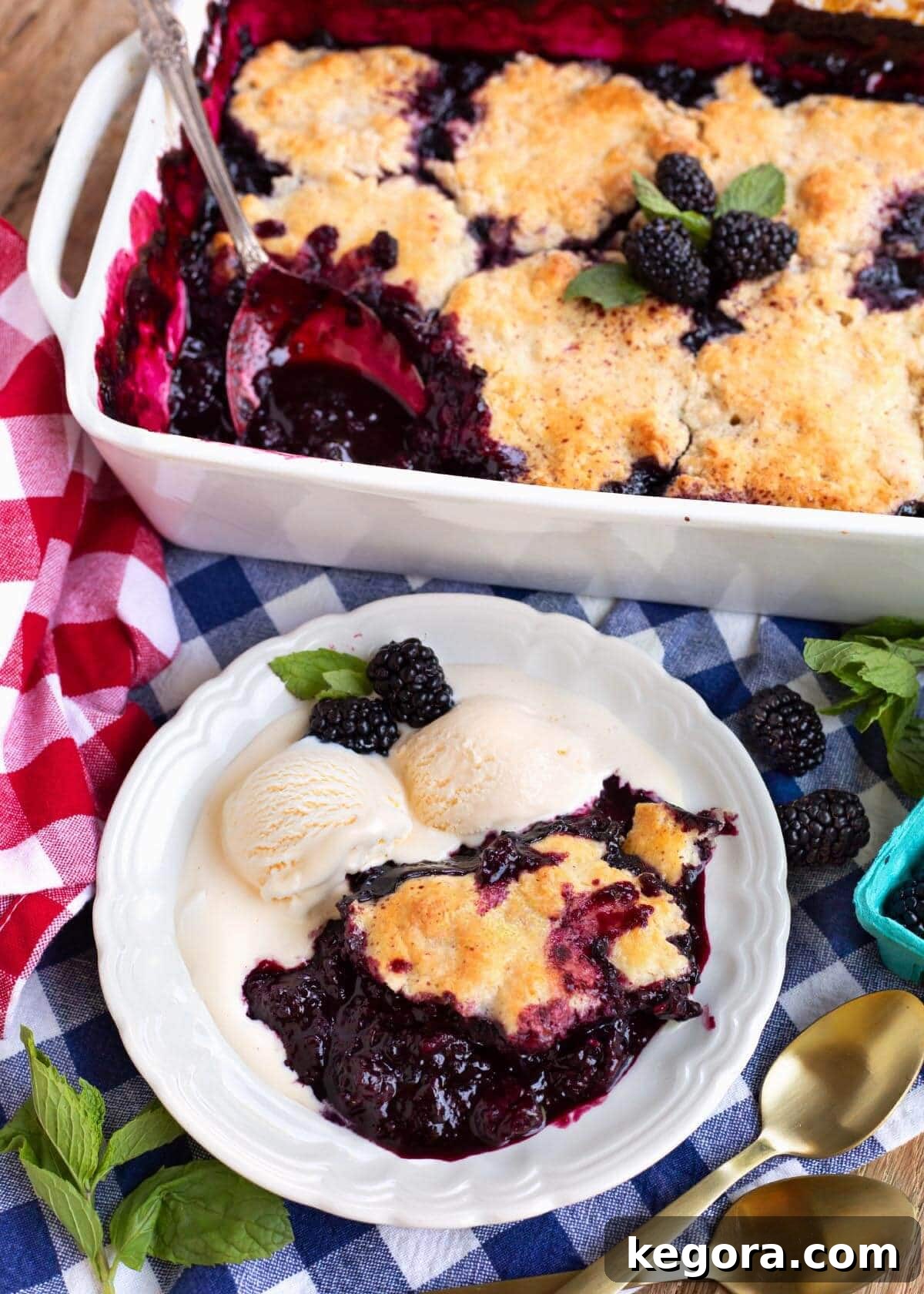 A warm slice of Homemade Blackberry Cobbler served on a white plate with a scoop of vanilla ice cream, showing the rich berry filling and golden biscuit topping.